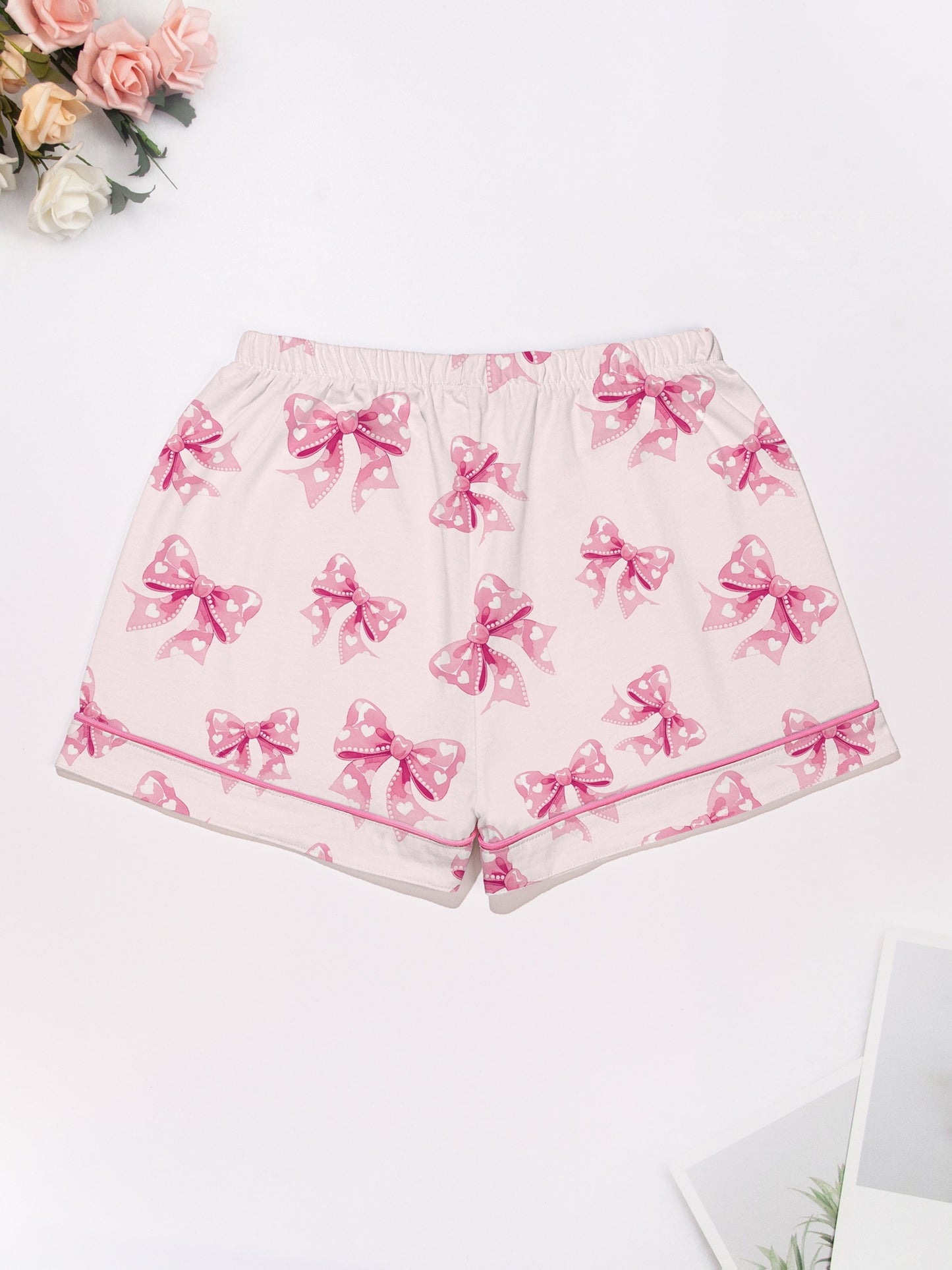 Pastel pink short-sleeve pajama set with heart-dotted bow print — button-up top and elastic waist shorts with pink piping