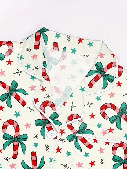 Cream cotton pajama set with candy‑cane and green bow print — short‑sleeve button top and elastic waist shorts with piping