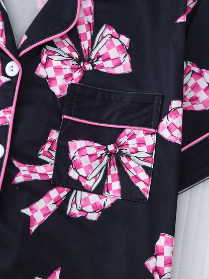 Black satin-look pajama set with pink-check bow print, piped trim, short sleeve button top and elastic waist shorts in silky stretch fabric — 95% Polyester/5% Elastane