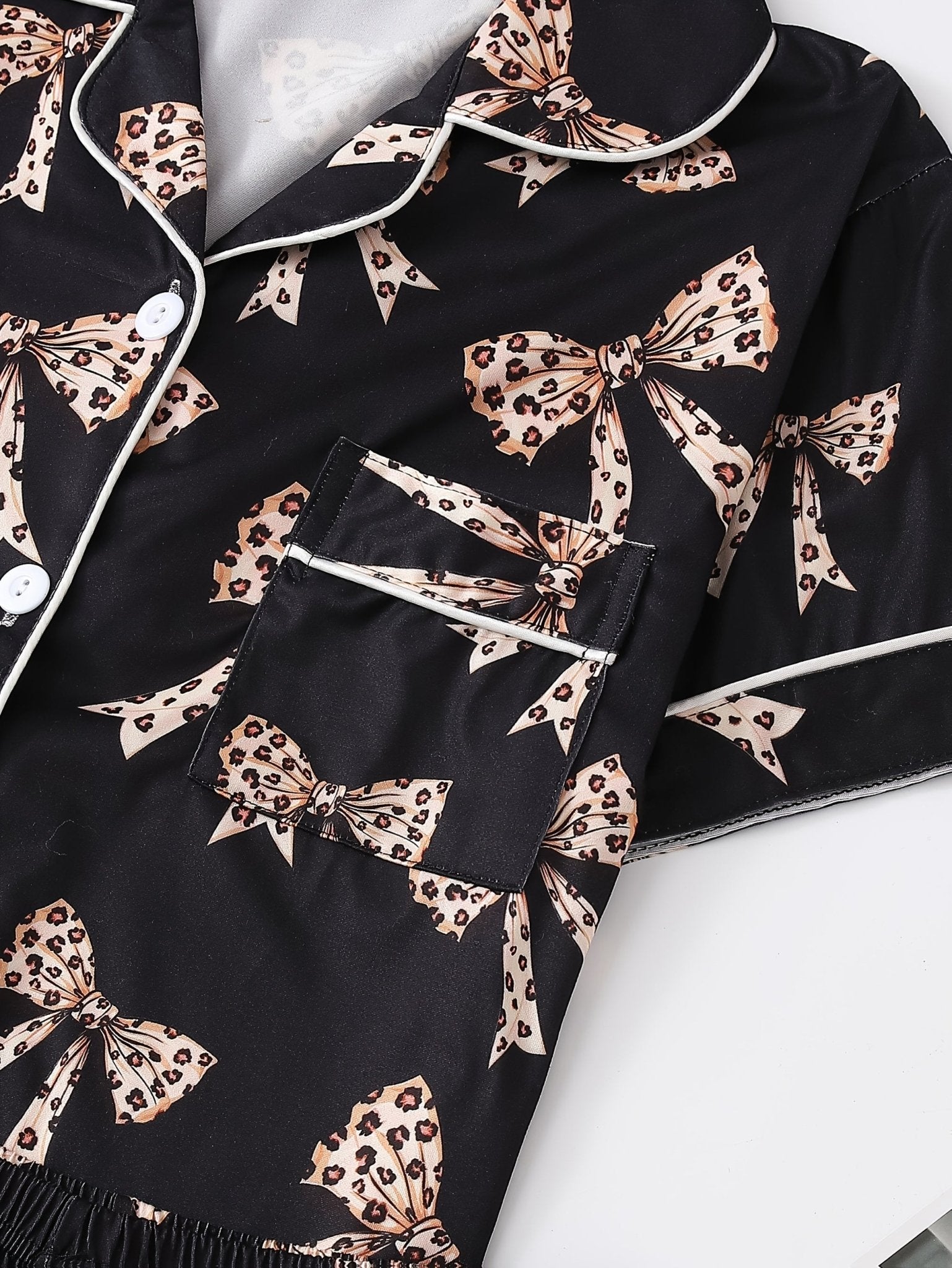 Black satin-look short-sleeve pajama set with beige leopard bow print, piped trim, chest pocket and elastic waist shorts in 95% Polyester 5% Elastane