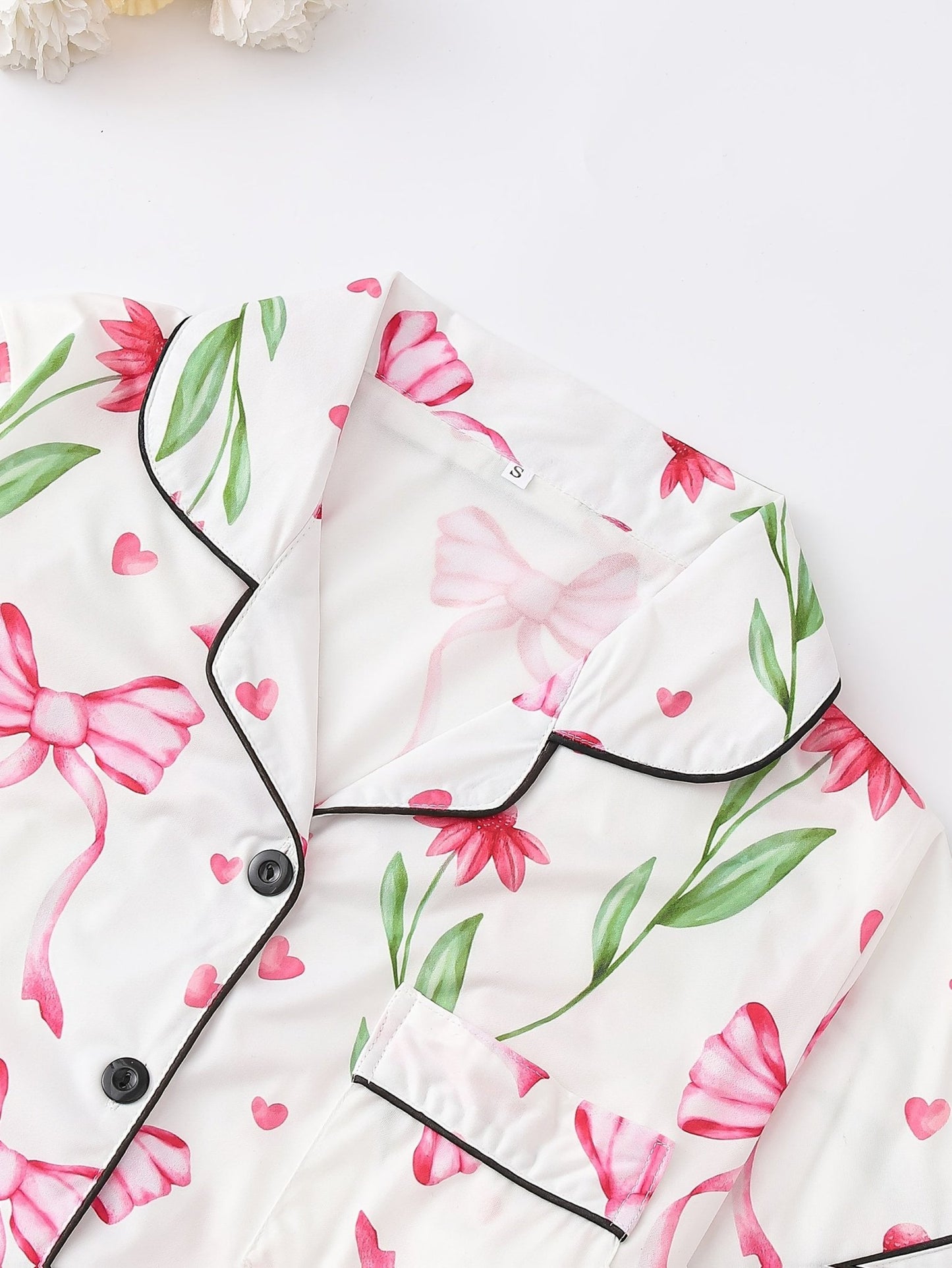 White satin-look short-sleeve pajama set with pink bow and floral print, piped trim, chest pocket and elastic waist shorts in 95% Polyester 5% Elastane — travel-ready silky stretch loungewear