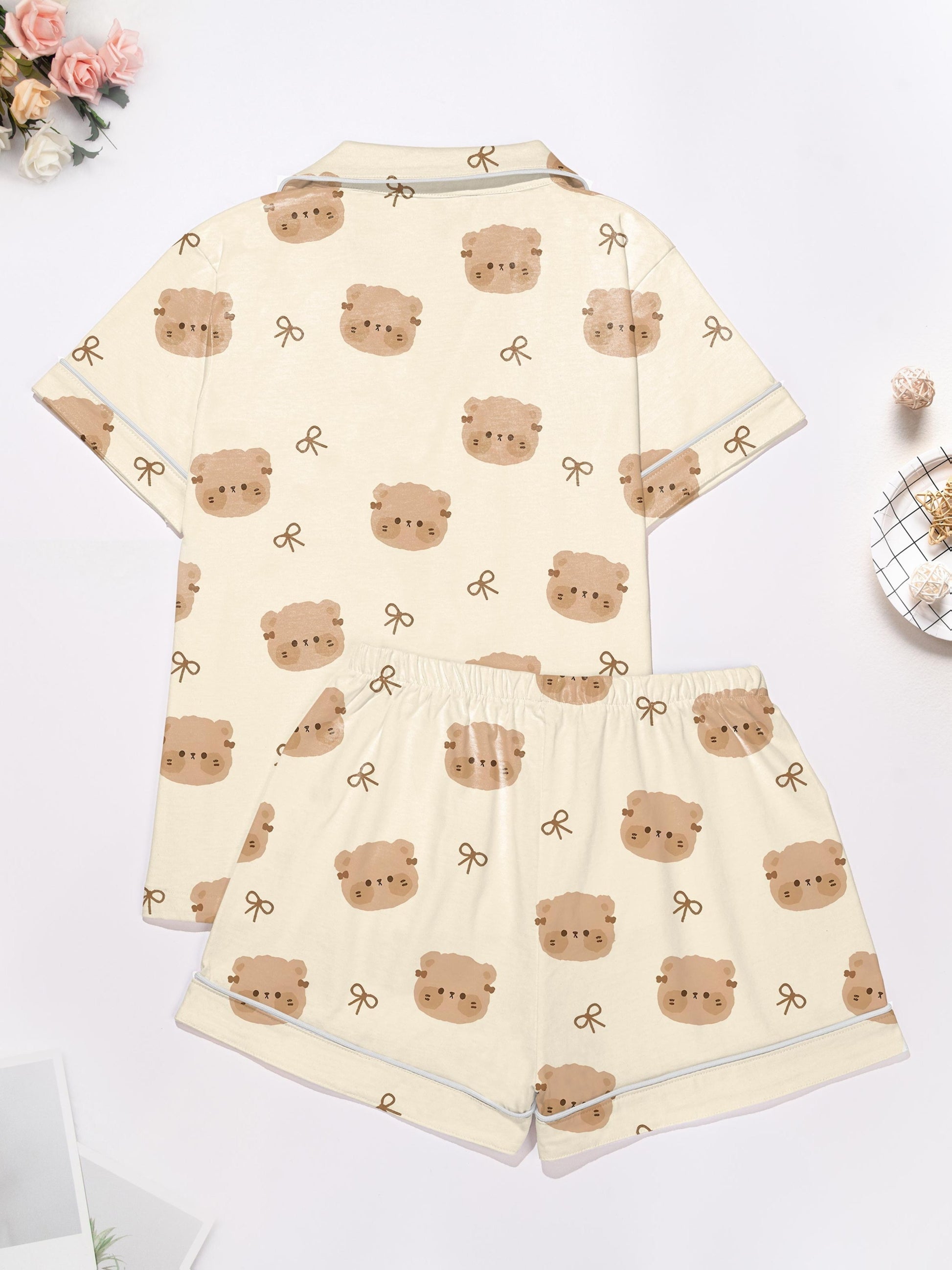 Cream short‑sleeve modal pajama set with teddy face and bow print — button‑up top and elastic waist shorts with piping