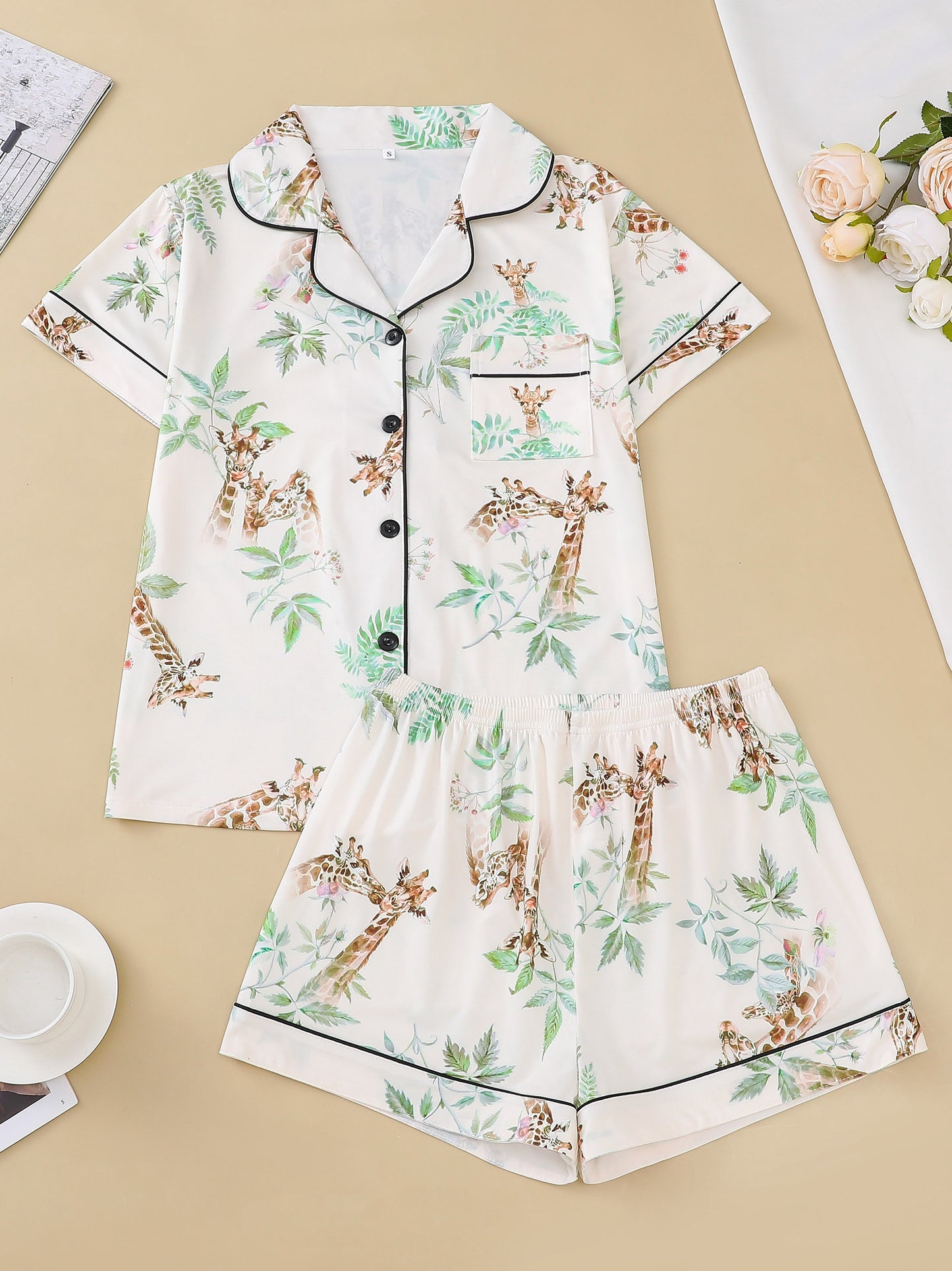 Cream satin-look pajama set with watercolor giraffe and green leaf print — short-sleeve button-up top with chest pocket and elastic waist shorts, 95% Polyester/5% Elastane