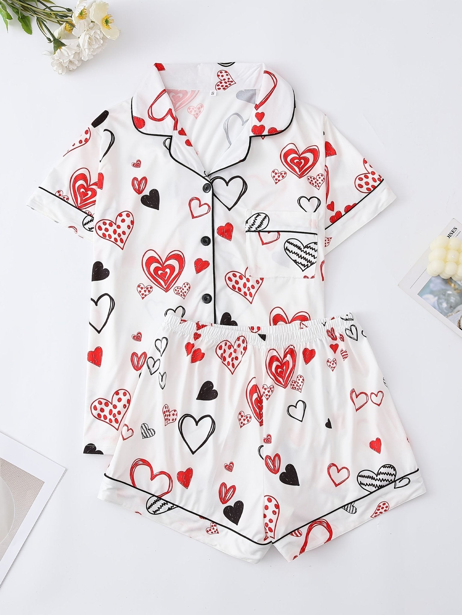 White satin-look short-sleeve pajama set with red and black hand-drawn heart print, piped trim, chest pocket and elastic waist shorts in 95% Polyester 5% Elastane — silky stretch travel-ready loungewear