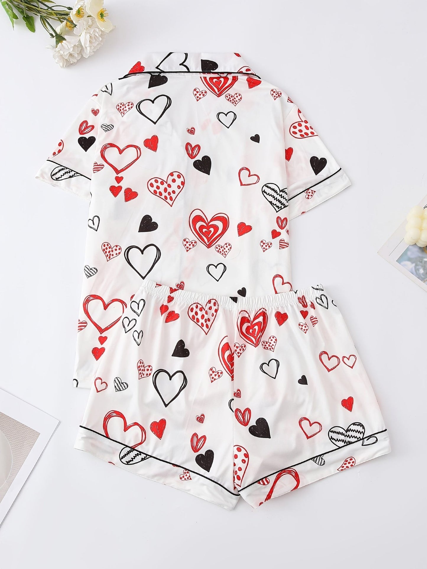 White satin-look short-sleeve pajama set with red and black hand-drawn heart print, piped trim, chest pocket and elastic waist shorts in 95% Polyester 5% Elastane — silky stretch travel-ready loungewear
