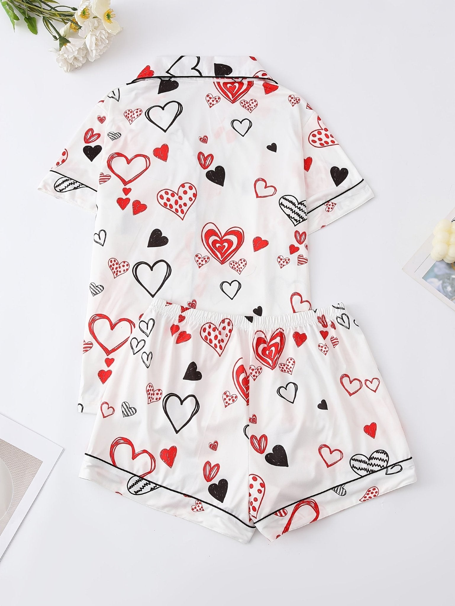 White satin-look short-sleeve pajama set with red and black hand-drawn heart print, piped trim, chest pocket and elastic waist shorts in 95% Polyester 5% Elastane — silky stretch travel-ready loungewear