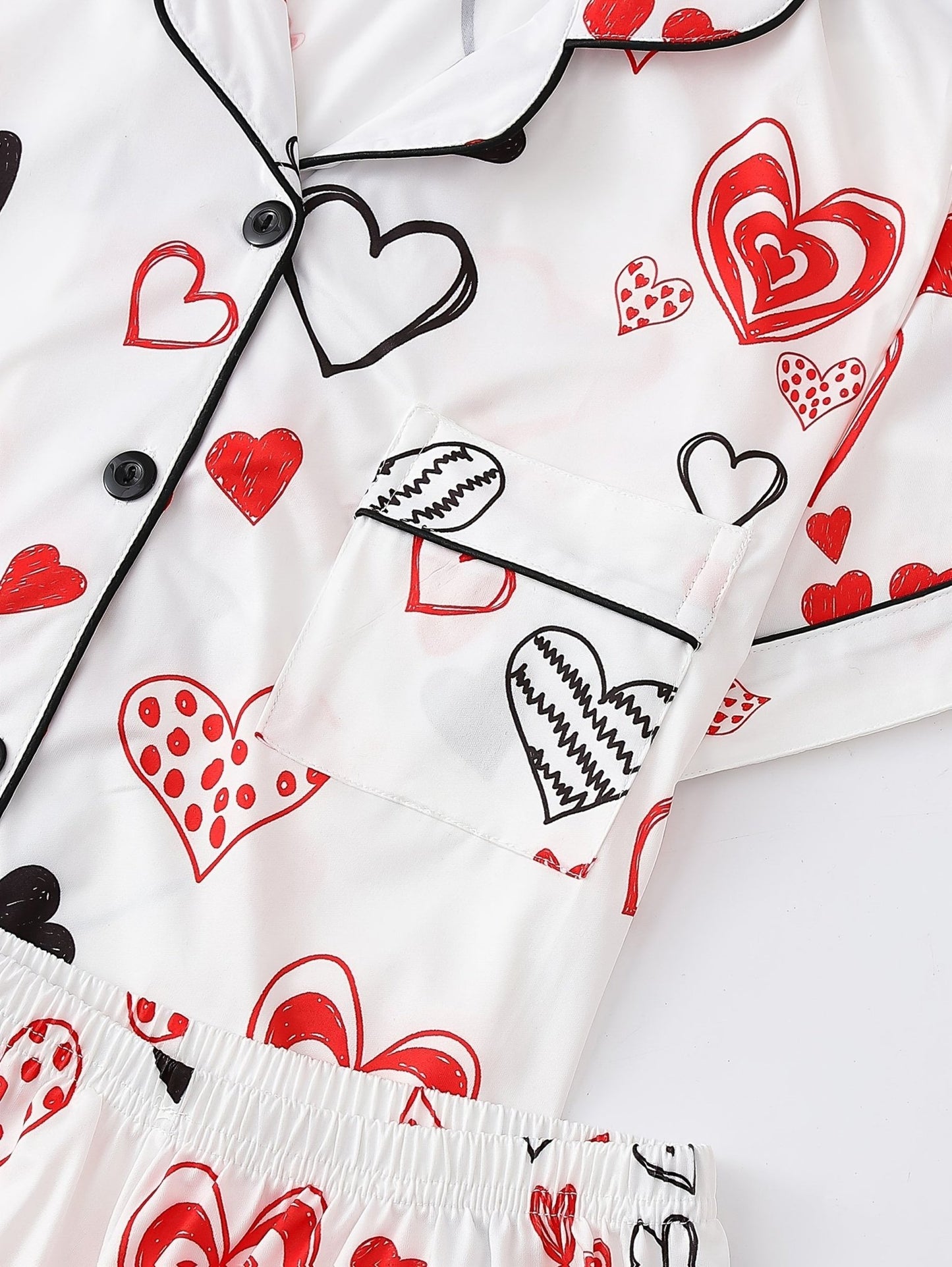 White satin-look short-sleeve pajama set with red and black hand-drawn heart print, piped trim, chest pocket and elastic waist shorts in 95% Polyester 5% Elastane — silky stretch travel-ready loungewear