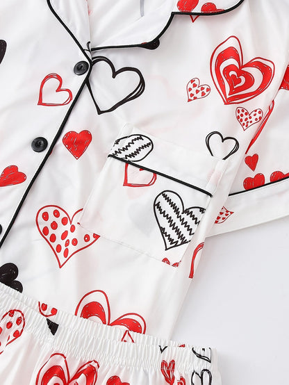 White satin-look short-sleeve pajama set with red and black hand-drawn heart print, piped trim, chest pocket and elastic waist shorts in 95% Polyester 5% Elastane — silky stretch travel-ready loungewear