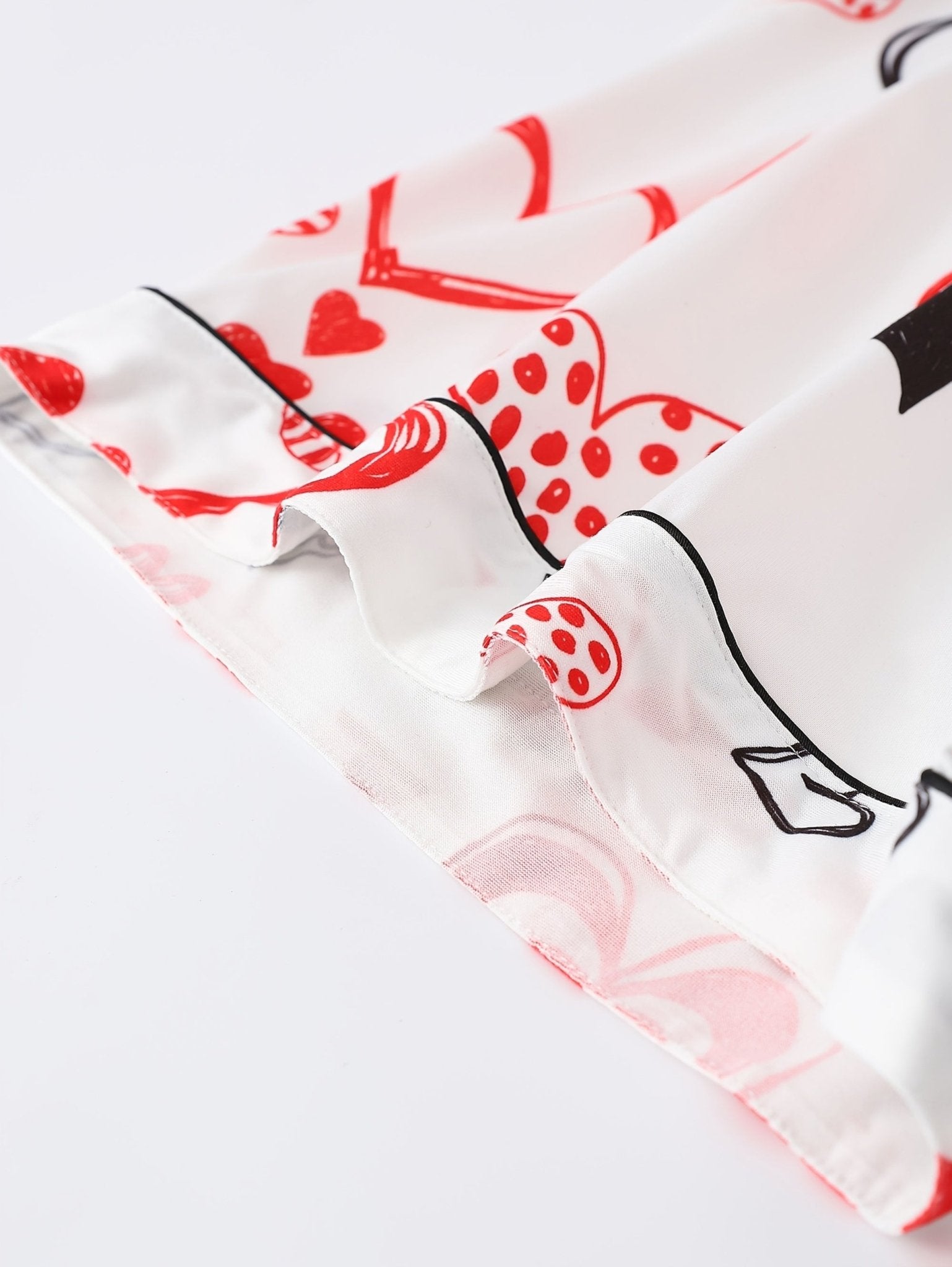 White satin-look short-sleeve pajama set with red and black hand-drawn heart print, piped trim, chest pocket and elastic waist shorts in 95% Polyester 5% Elastane — silky stretch travel-ready loungewear