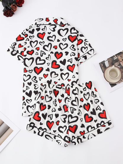 White satin-look short-sleeve pajama set with red and black heart print, piped trim, chest pocket and elastic waist shorts in 95% Polyester 5% Elastane — silky stretch travel-ready loungewear