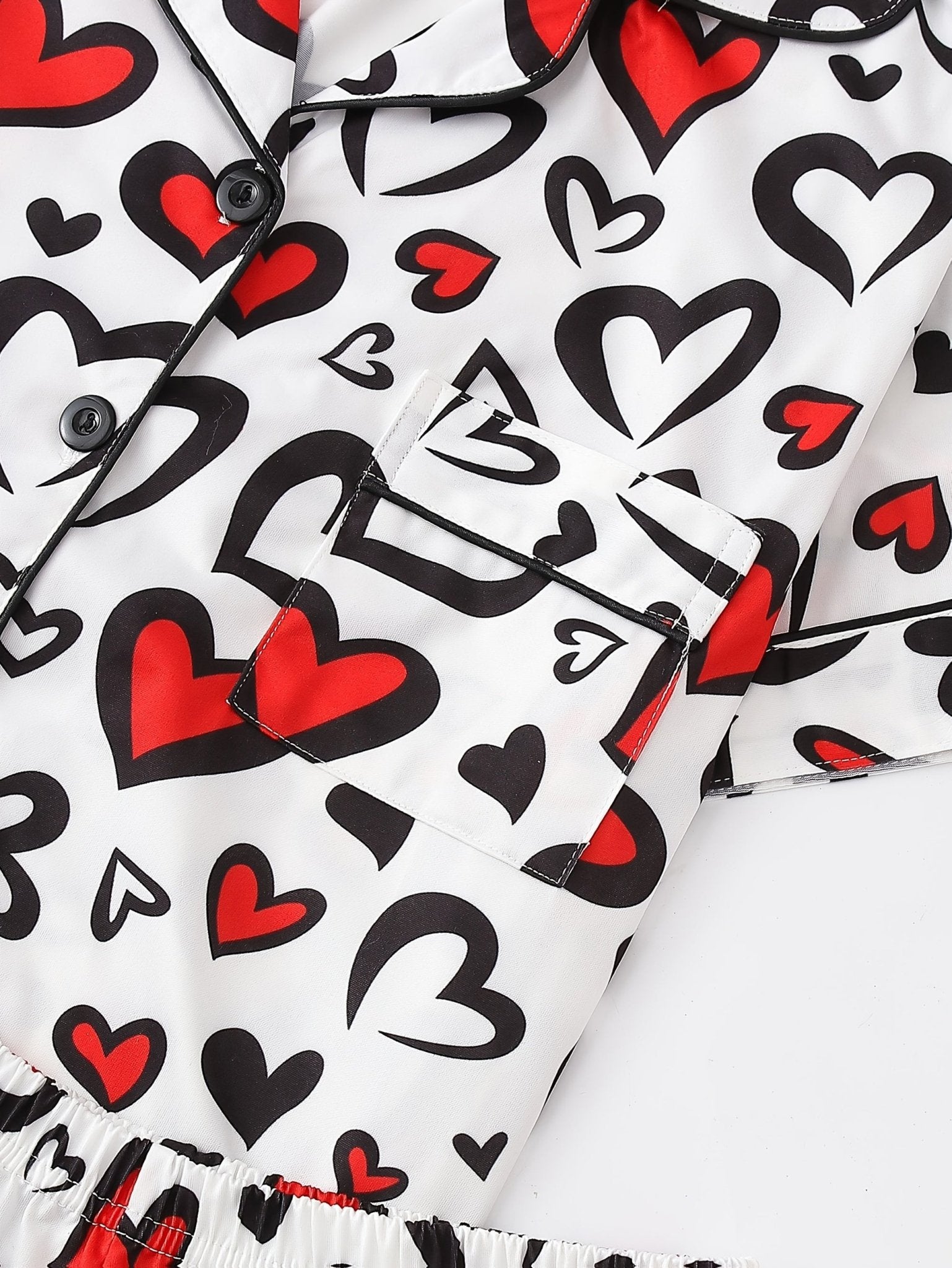 White satin-look short-sleeve pajama set with red and black heart print, piped trim, chest pocket and elastic waist shorts in 95% Polyester 5% Elastane — silky stretch travel-ready loungewear