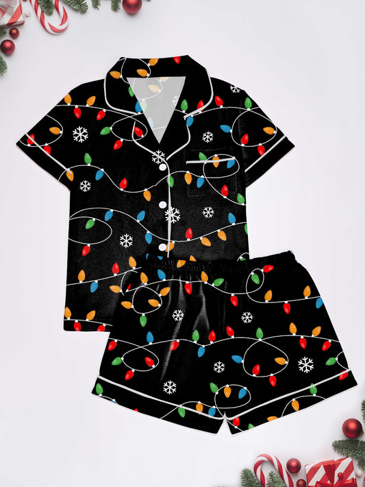 Black short-sleeve women’s pajama set with multicolor string-light and snowflake print — button-up top and elastic waist shorts with contrast piping
