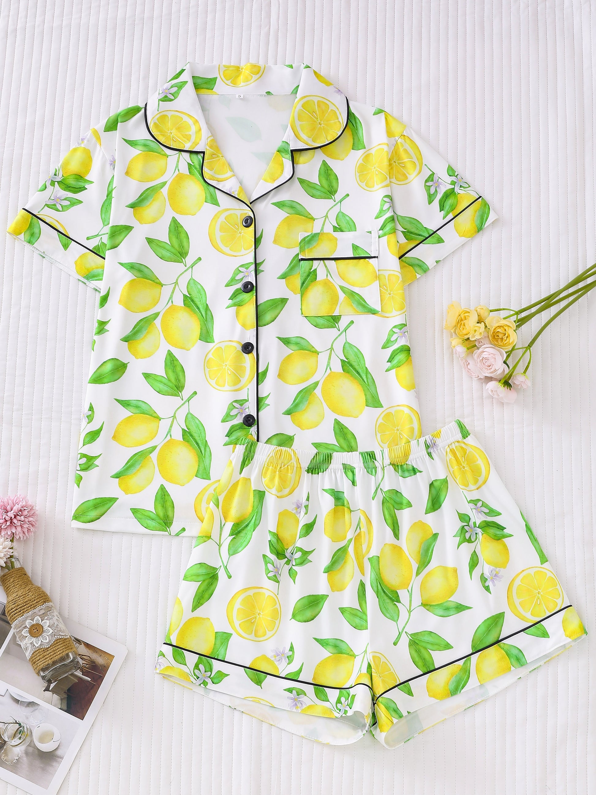 White satin-look pajama set with bright yellow lemon and green leaf print — short-sleeve button-up top with chest pocket and elastic waist shorts, 95% Polyester/5% Elastane