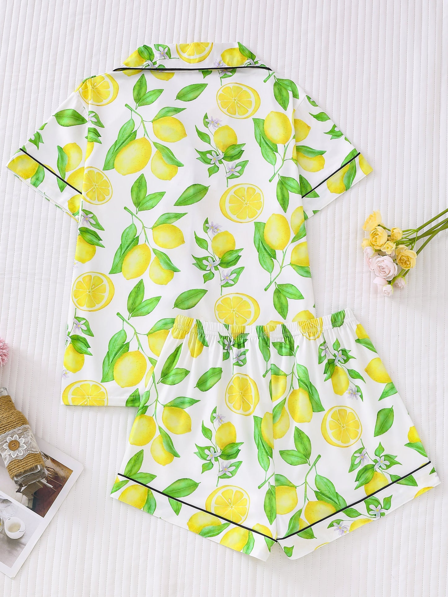 White satin-look pajama set with bright yellow lemon and green leaf print — short-sleeve button-up top with chest pocket and elastic waist shorts, 95% Polyester/5% Elastane