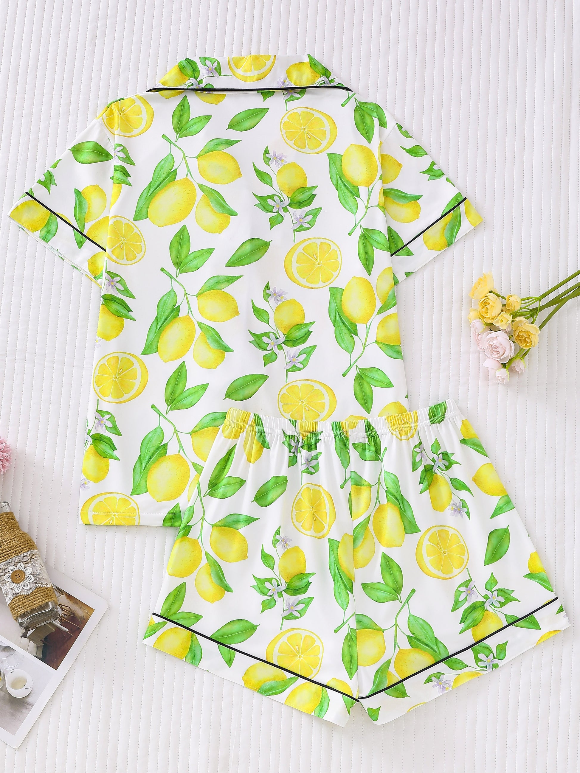 White satin-look pajama set with bright yellow lemon and green leaf print — short-sleeve button-up top with chest pocket and elastic waist shorts, 95% Polyester/5% Elastane
