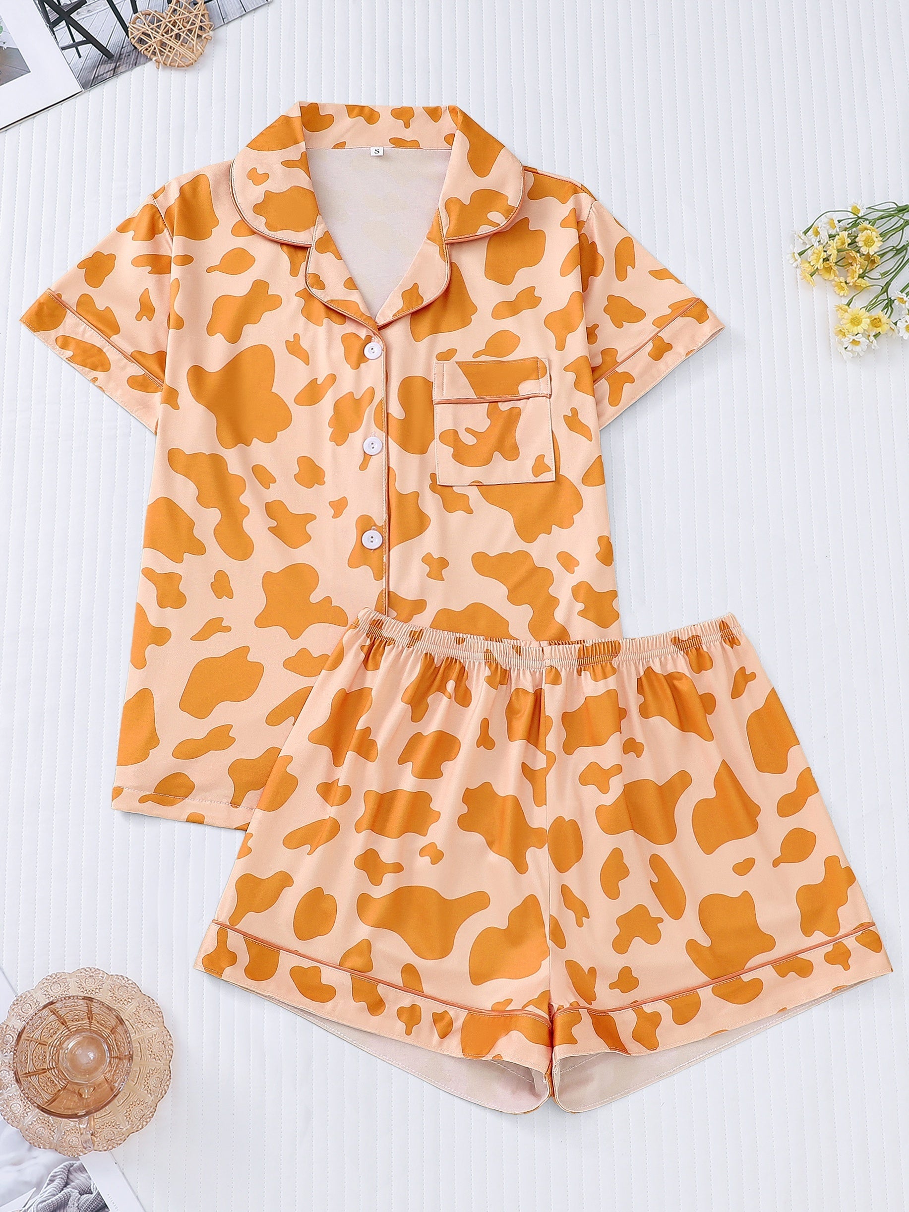 White silk‑touch modal short‑sleeve pajama top and elastic waist shorts with black cow‑spot print and aqua piping