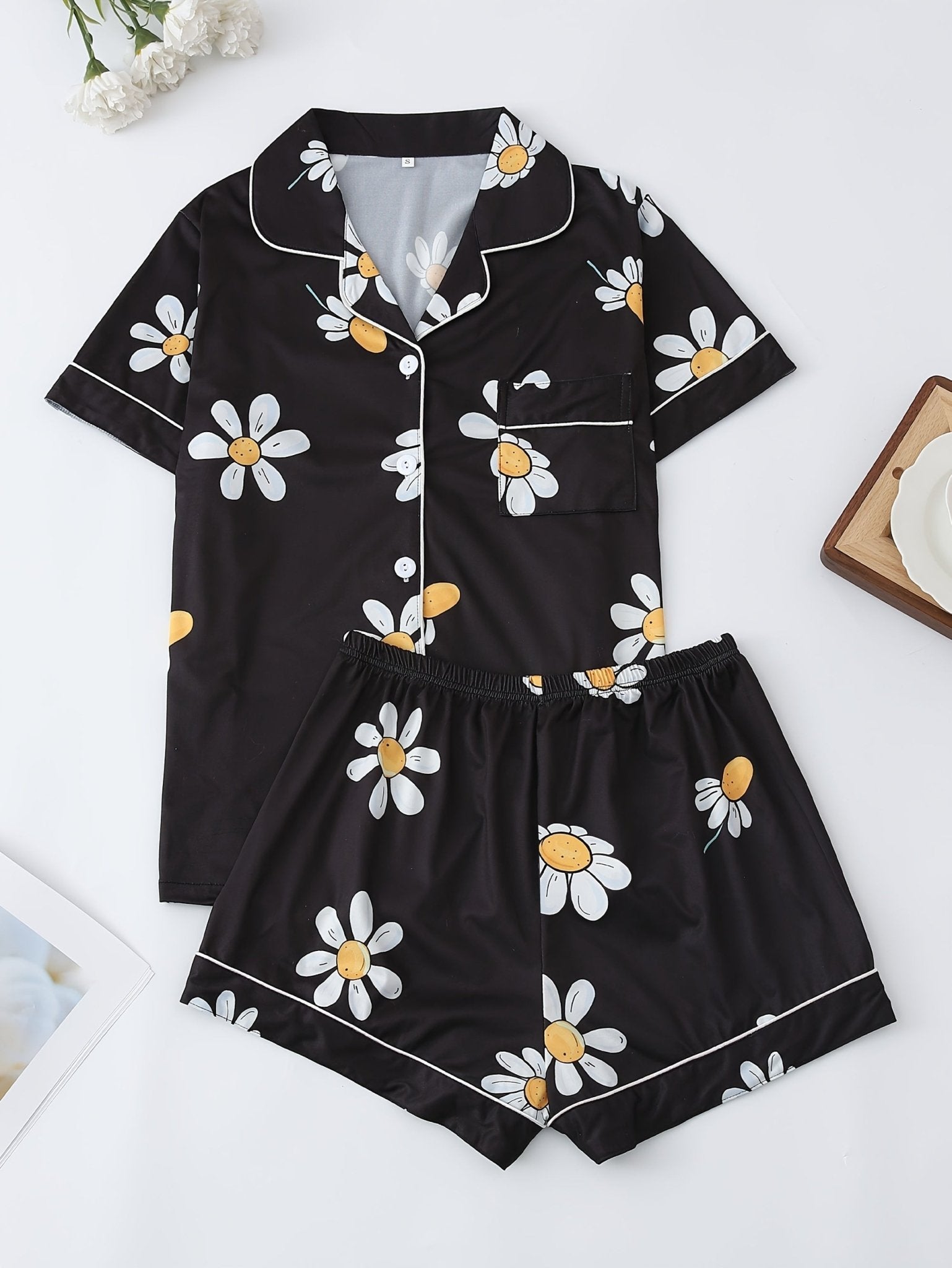 Black satin-look short-sleeve pajama set with white daisy print, piped trim, chest pocket and elastic waist shorts in 95% Polyester 5% Elastane — silky stretch loungewear