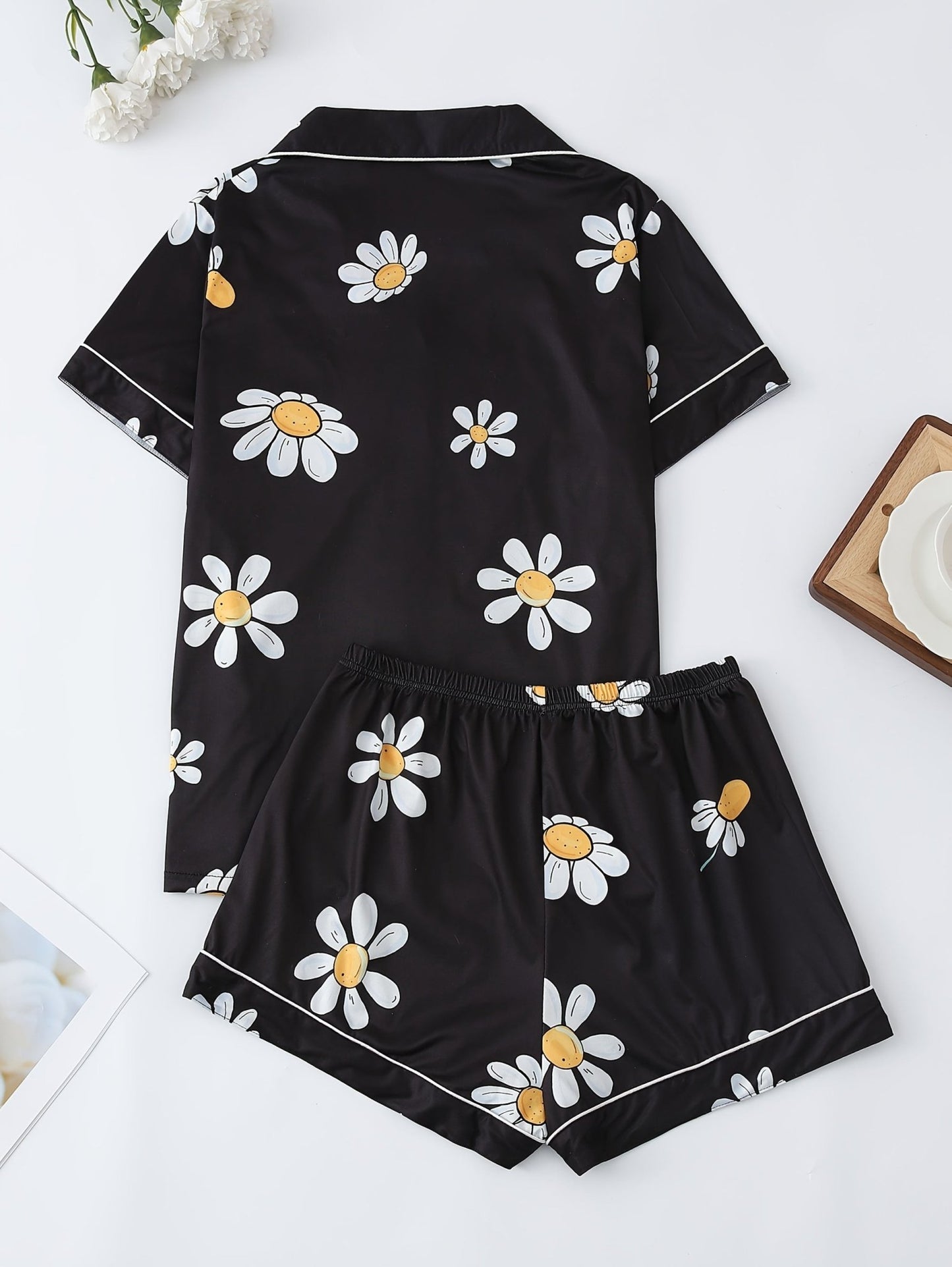 Black satin-look short-sleeve pajama set with white daisy print, piped trim, chest pocket and elastic waist shorts in 95% Polyester 5% Elastane — silky stretch loungewear