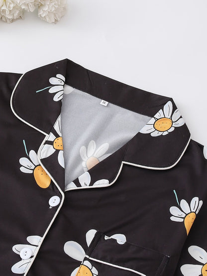 Black satin-look short-sleeve pajama set with white daisy print, piped trim, chest pocket and elastic waist shorts in 95% Polyester 5% Elastane — silky stretch loungewear