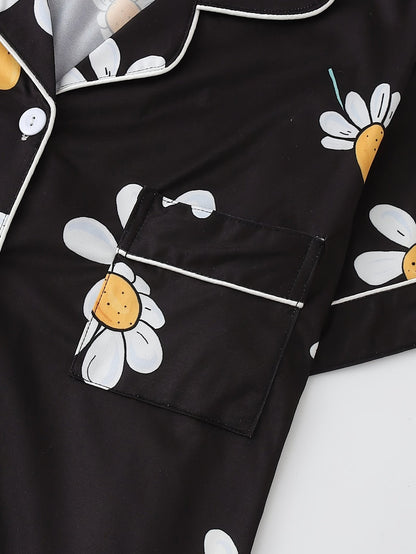 Black satin-look short-sleeve pajama set with white daisy print, piped trim, chest pocket and elastic waist shorts in 95% Polyester 5% Elastane — silky stretch loungewear