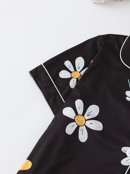 Black satin-look short-sleeve pajama set with white daisy print, piped trim, chest pocket and elastic waist shorts in 95% Polyester 5% Elastane — silky stretch loungewear