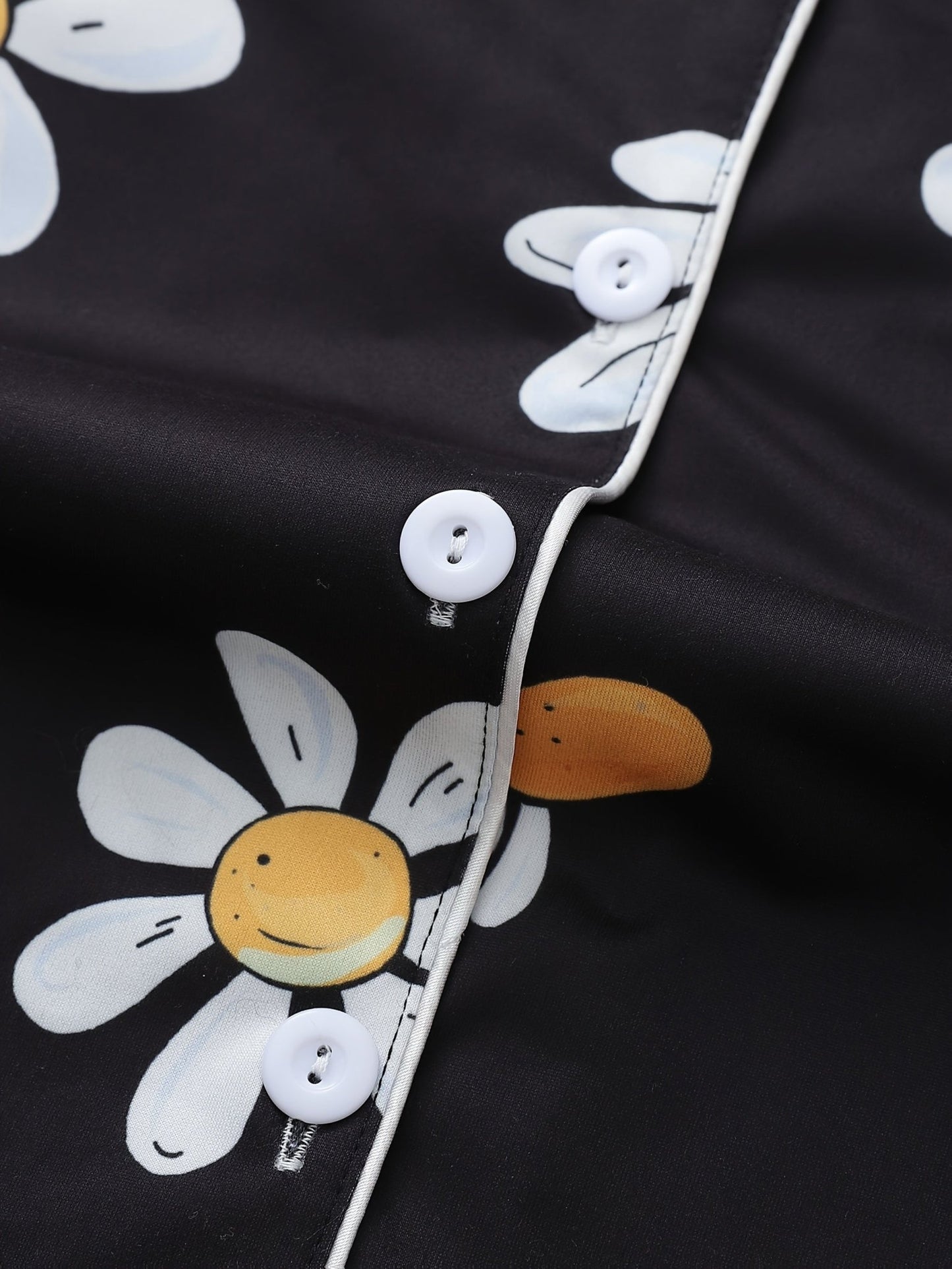 Black satin-look short-sleeve pajama set with white daisy print, piped trim, chest pocket and elastic waist shorts in 95% Polyester 5% Elastane — silky stretch loungewear