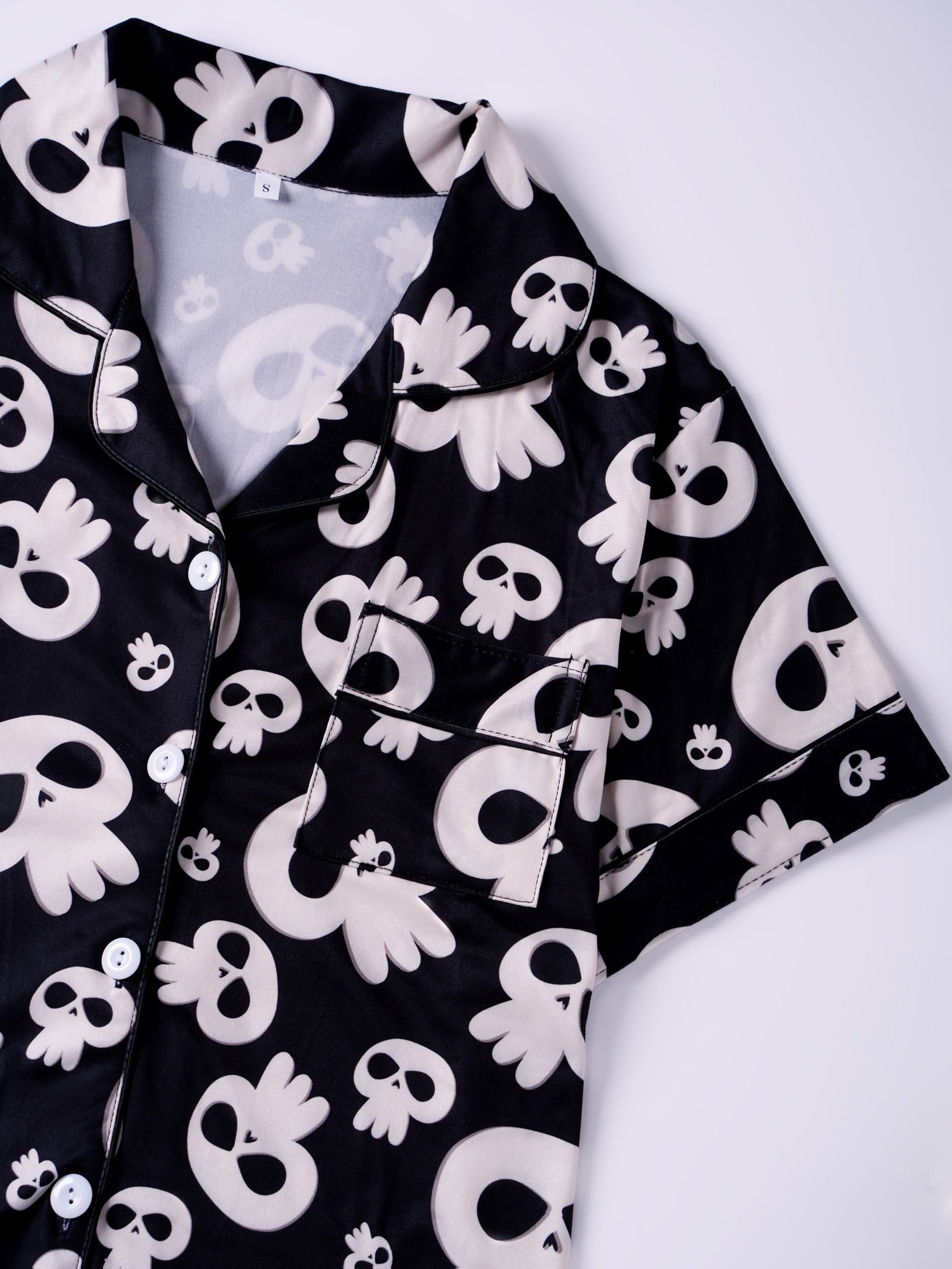 Black modal pajama set with cream skull motifs — short‑sleeve button top and elastic waist shorts with piping
