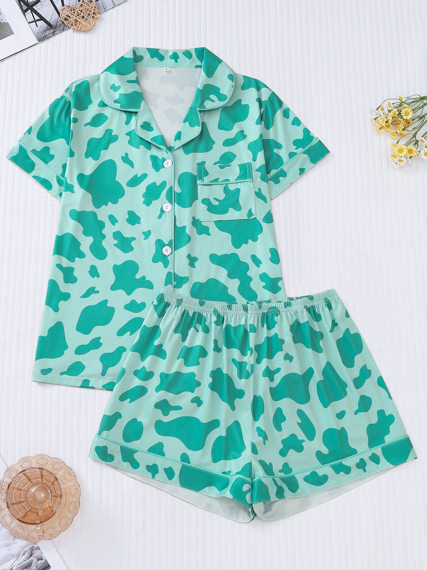 White silk‑touch modal short‑sleeve pajama top and elastic waist shorts with black cow‑spot print and aqua piping