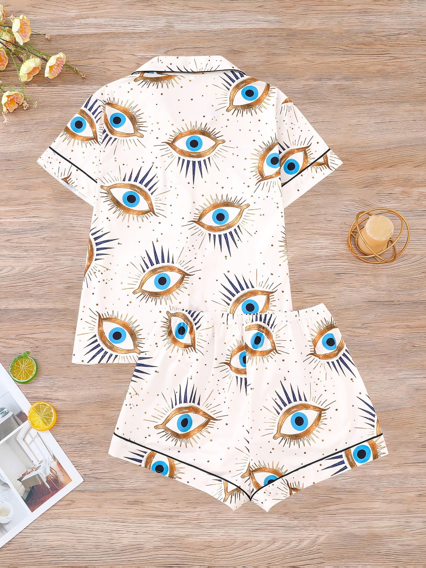 Cream satin-look pajama set with blue and gold guardian-eye print — short-sleeve button-up top with chest pocket and elastic waist shorts, 95% Polyester/5% Elastane