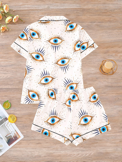 Cream satin-look pajama set with blue and gold guardian-eye print — short-sleeve button-up top with chest pocket and elastic waist shorts, 95% Polyester/5% Elastane