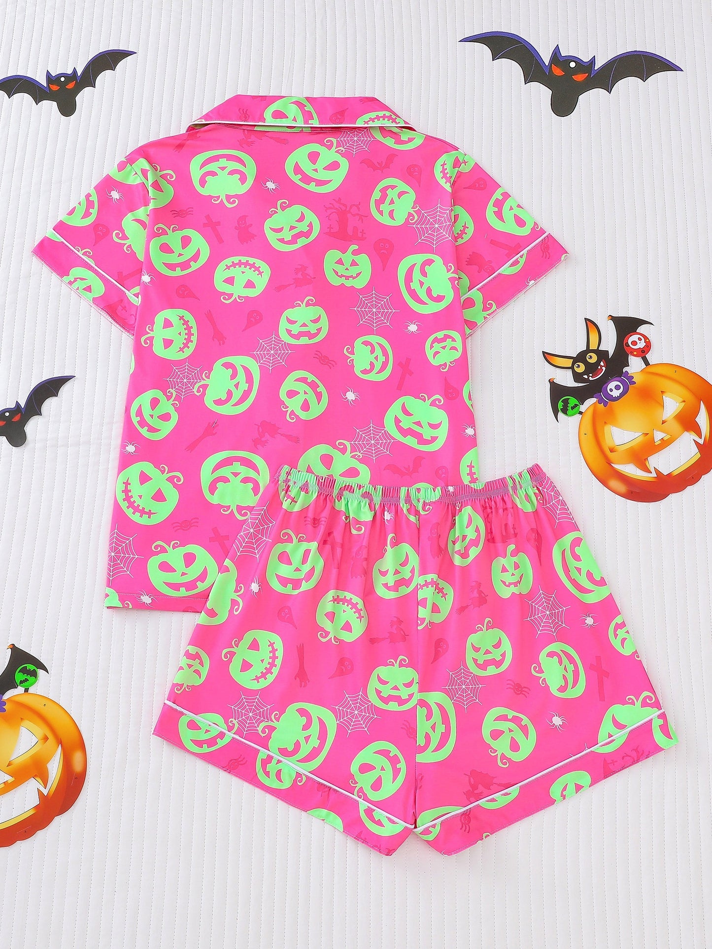 Hot-pink satin-look short pajama set with neon lime pumpkin jack-o’-lanterns and spiderweb print — short-sleeve relaxed top and elastic waist shorts, 95% Polyester/5% Elastane, lightweight and breathable