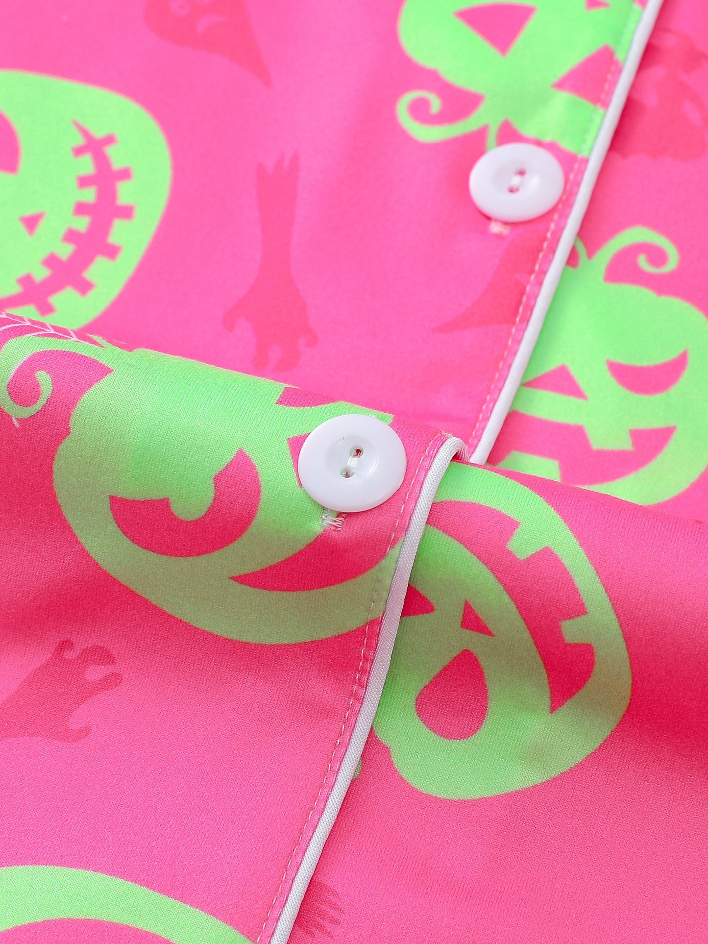 Hot-pink satin-look short pajama set with neon lime pumpkin jack-o’-lanterns and spiderweb print — short-sleeve relaxed top and elastic waist shorts, 95% Polyester/5% Elastane, lightweight and breathable