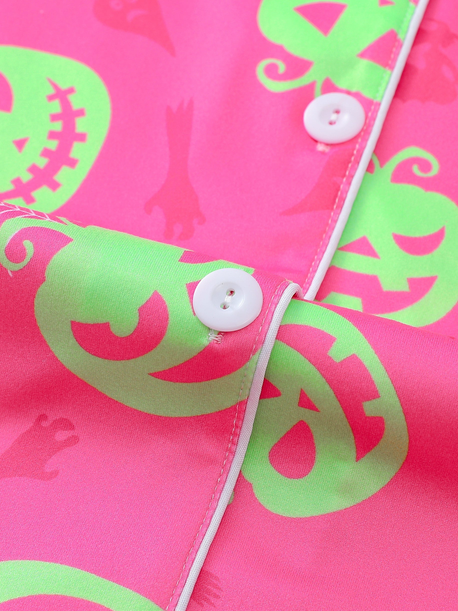 Hot-pink satin-look short pajama set with neon lime pumpkin jack-o’-lanterns and spiderweb print — short-sleeve relaxed top and elastic waist shorts, 95% Polyester/5% Elastane, lightweight and breathable