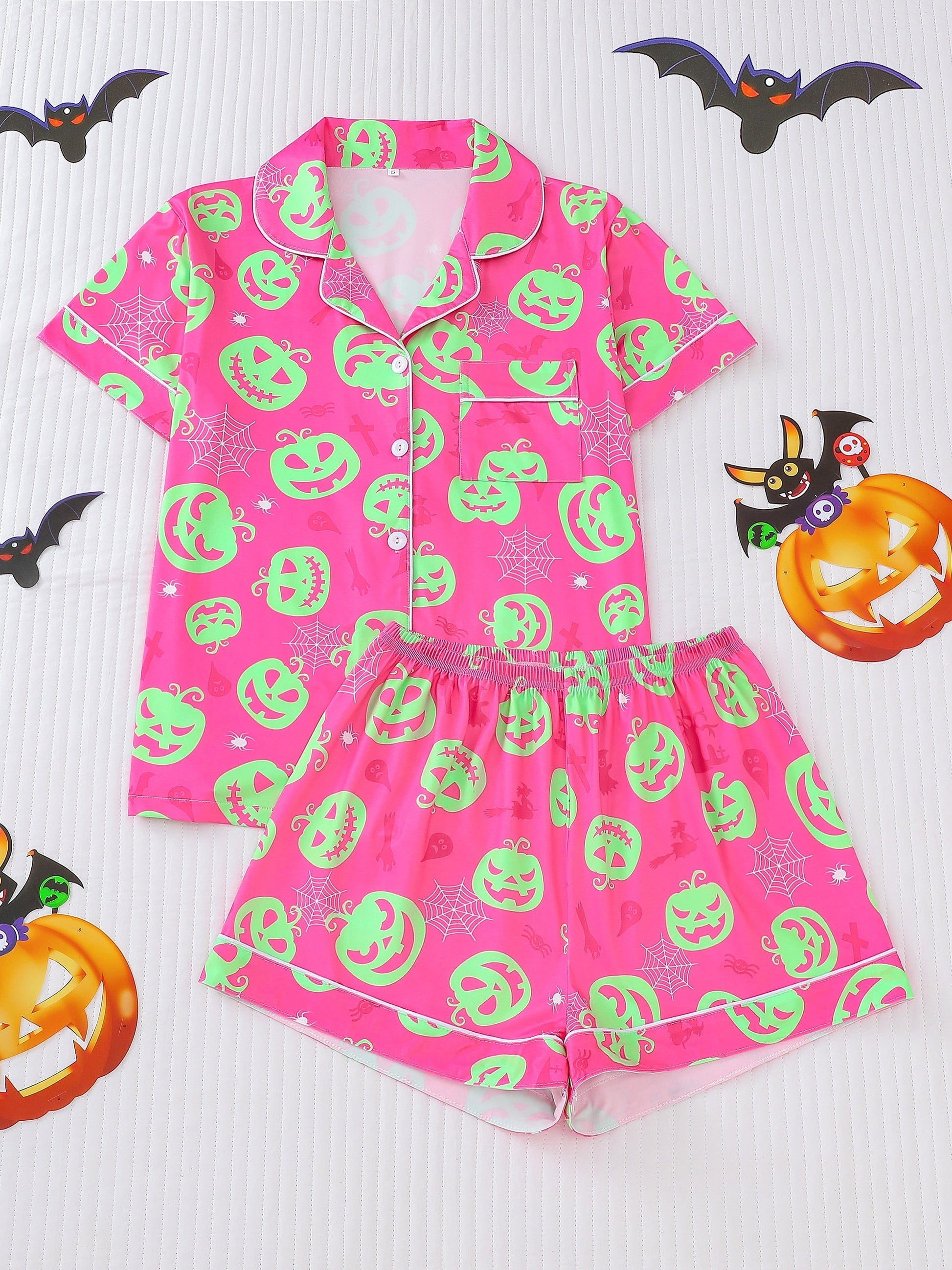Hot-pink satin-look short pajama set with neon lime pumpkin jack-o’-lanterns and spiderweb print — short-sleeve relaxed top and elastic waist shorts, 95% Polyester/5% Elastane, lightweight and breathable