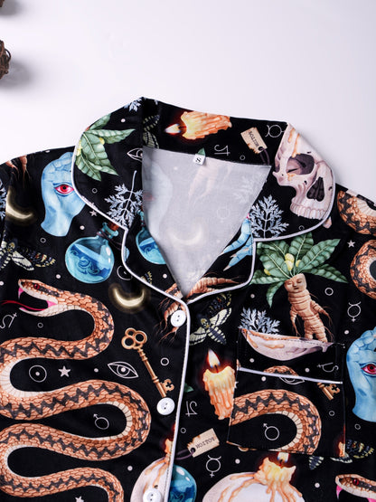 Black satin‑look pajama set with skulls, serpents, potion vials and botanicals — short‑sleeve button‑up top with chest pocket and elastic waist shorts with white piping