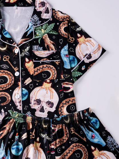 Black satin‑look pajama set with skulls, serpents, potion vials and botanicals — short‑sleeve button‑up top with chest pocket and elastic waist shorts with white piping