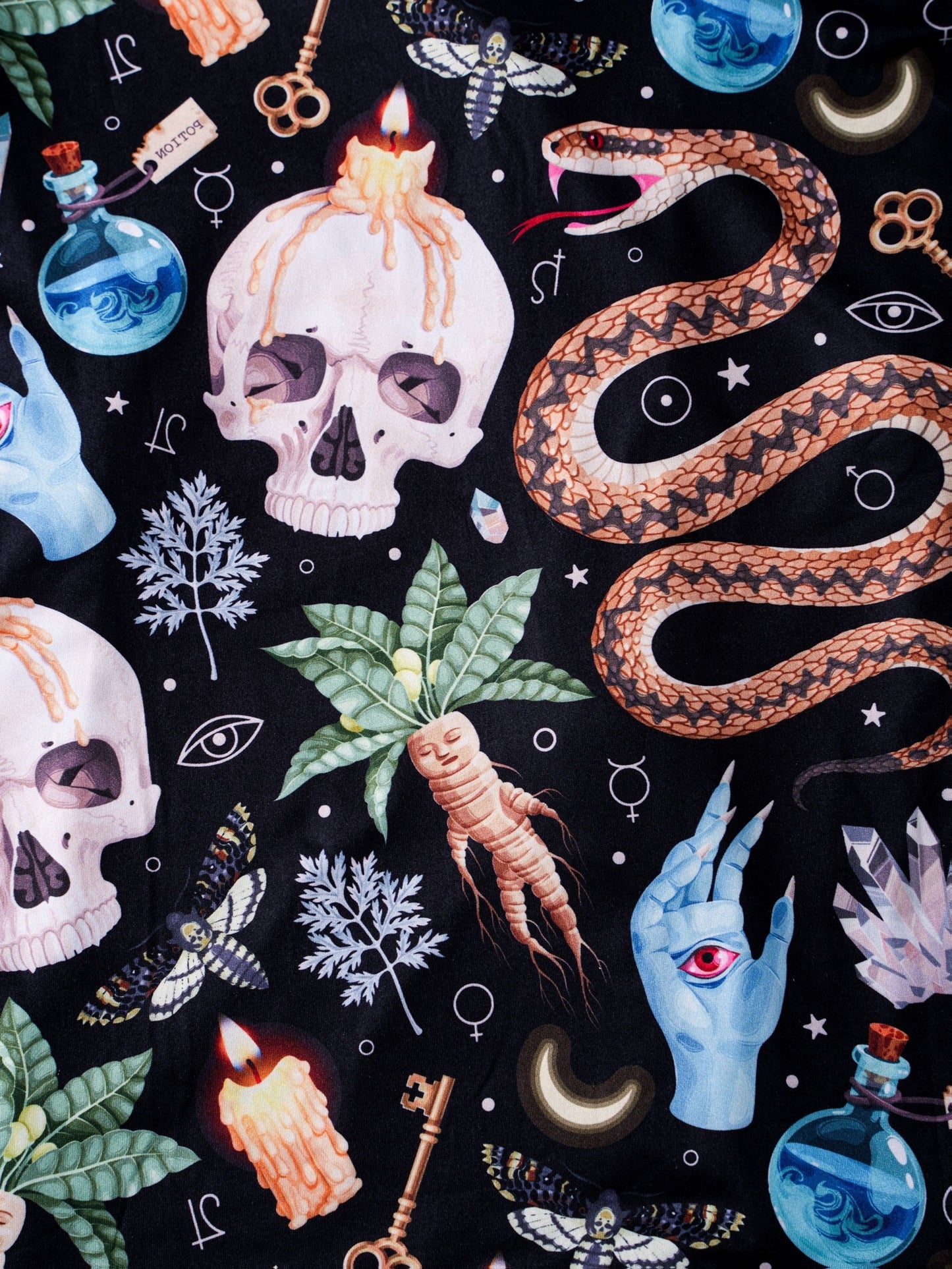 Black satin‑look pajama set with skulls, serpents, potion vials and botanicals — short‑sleeve button‑up top with chest pocket and elastic waist shorts with white piping