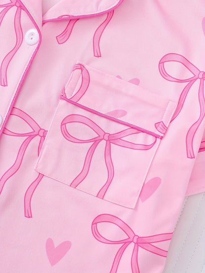 Pink satin-look short sleeve pajama set with bow print and hearts, piped trim, chest pocket and elastic waist shorts in 95% Polyester 5% Elastane — silky stretch loungewear