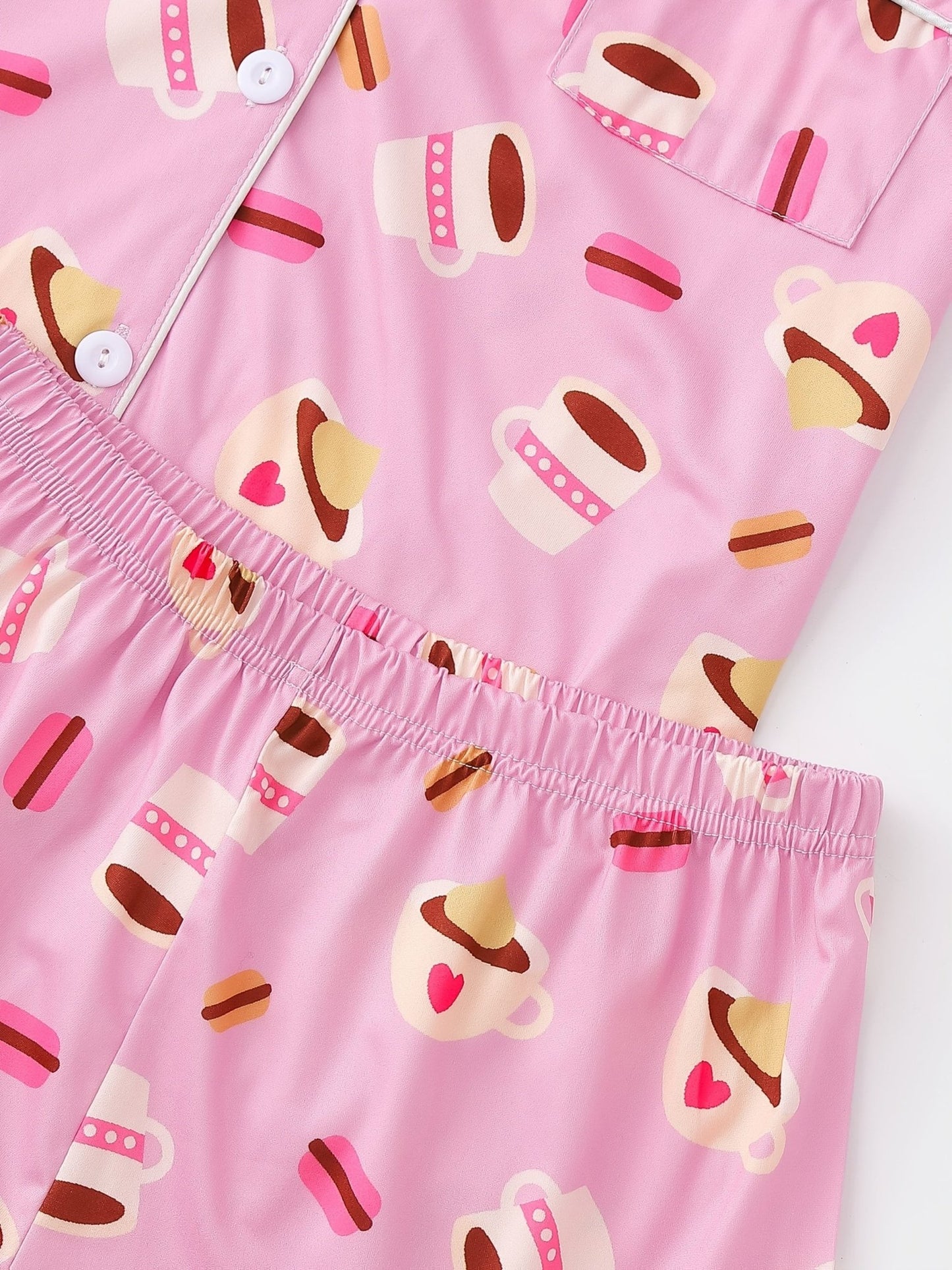 Pink satin-look short-sleeve pajama set with coffee cup and macaron print, piped trim, chest pocket and elastic waist shorts in 95% Polyester 5% Elastane — silky stretch travel-ready loungewear