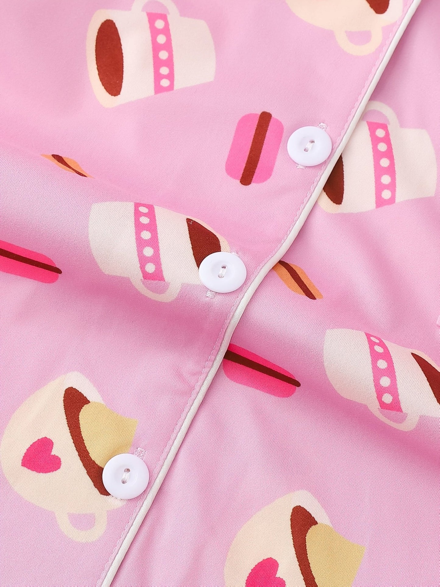 Pink satin-look short-sleeve pajama set with coffee cup and macaron print, piped trim, chest pocket and elastic waist shorts in 95% Polyester 5% Elastane — silky stretch travel-ready loungewear