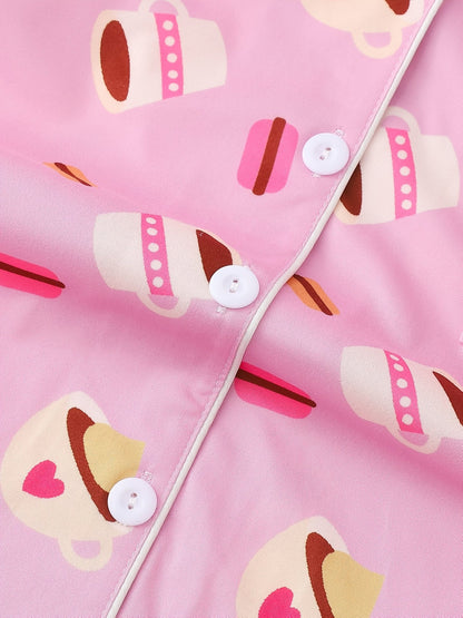 Pink satin-look short-sleeve pajama set with coffee cup and macaron print, piped trim, chest pocket and elastic waist shorts in 95% Polyester 5% Elastane — silky stretch travel-ready loungewear