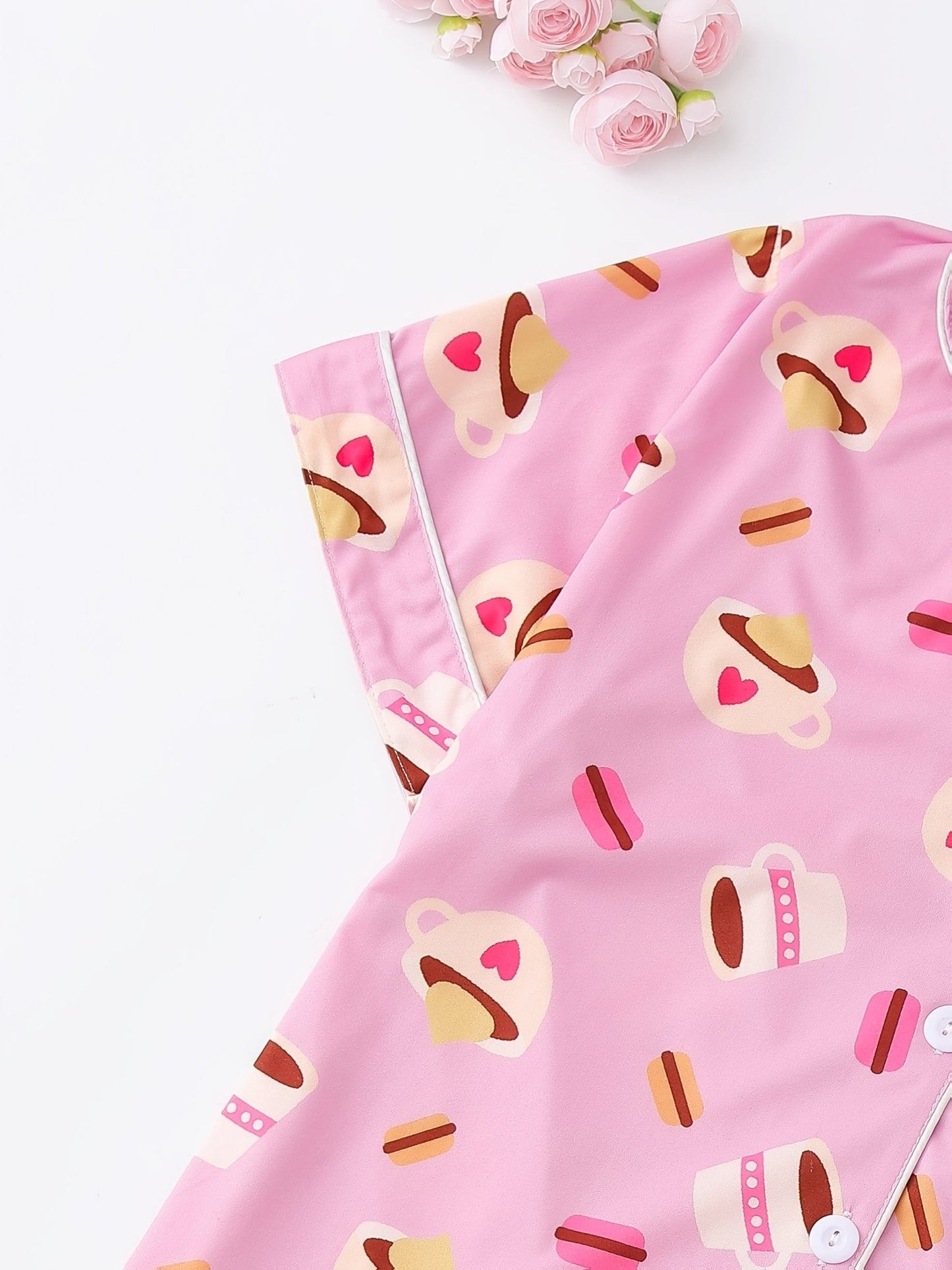Pink satin-look short-sleeve pajama set with coffee cup and macaron print, piped trim, chest pocket and elastic waist shorts in 95% Polyester 5% Elastane — silky stretch travel-ready loungewear
