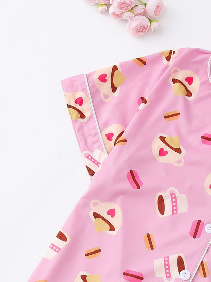 Pink satin-look short-sleeve pajama set with coffee cup and macaron print, piped trim, chest pocket and elastic waist shorts in 95% Polyester 5% Elastane — silky stretch travel-ready loungewear