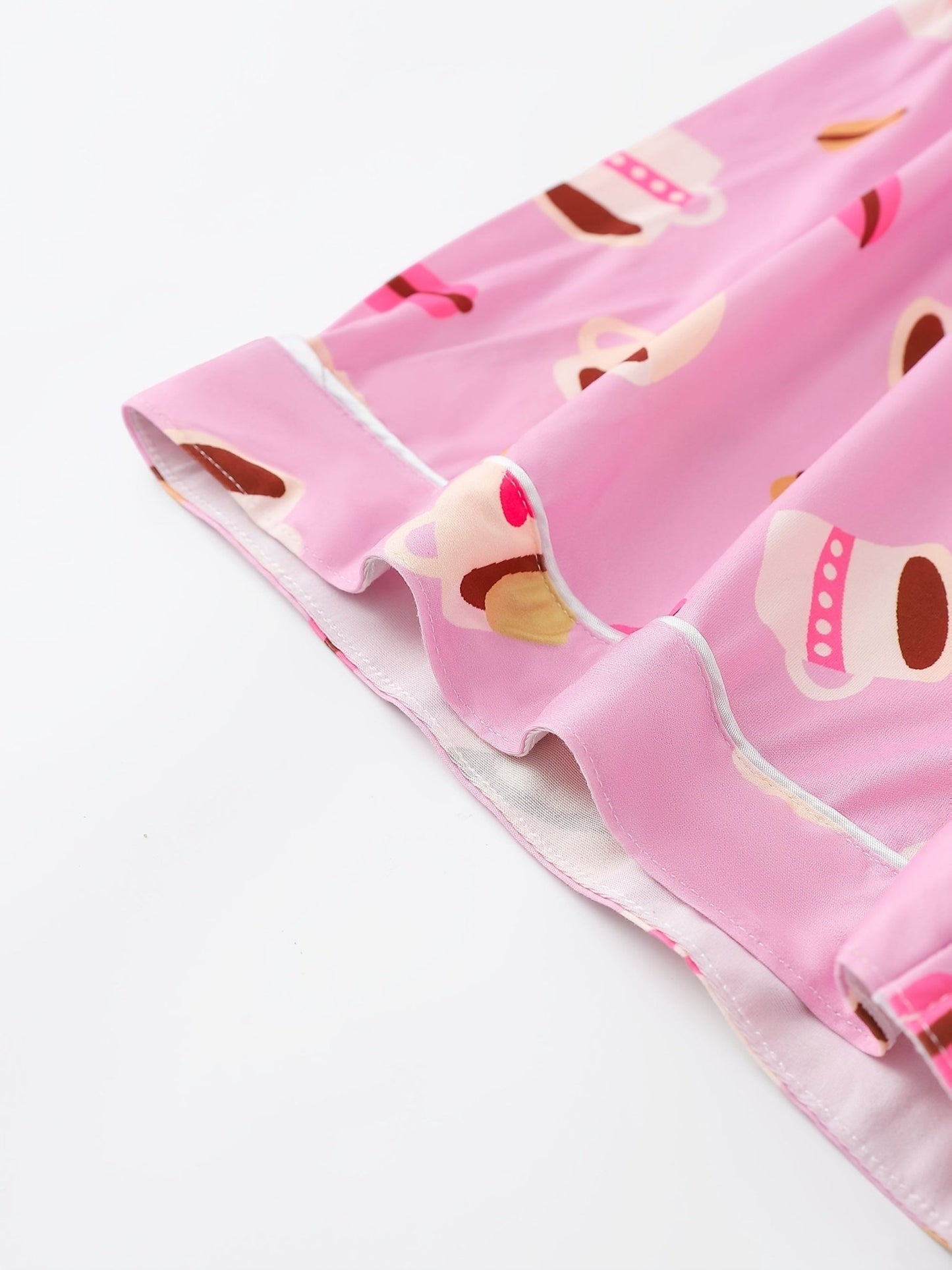 Pink satin-look short-sleeve pajama set with coffee cup and macaron print, piped trim, chest pocket and elastic waist shorts in 95% Polyester 5% Elastane — silky stretch travel-ready loungewear