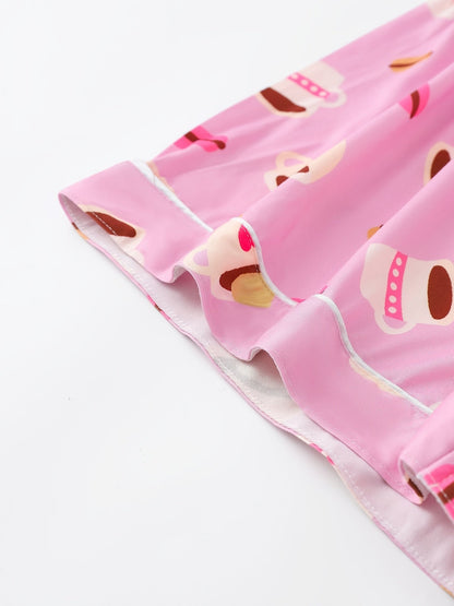 Pink satin-look short-sleeve pajama set with coffee cup and macaron print, piped trim, chest pocket and elastic waist shorts in 95% Polyester 5% Elastane — silky stretch travel-ready loungewear