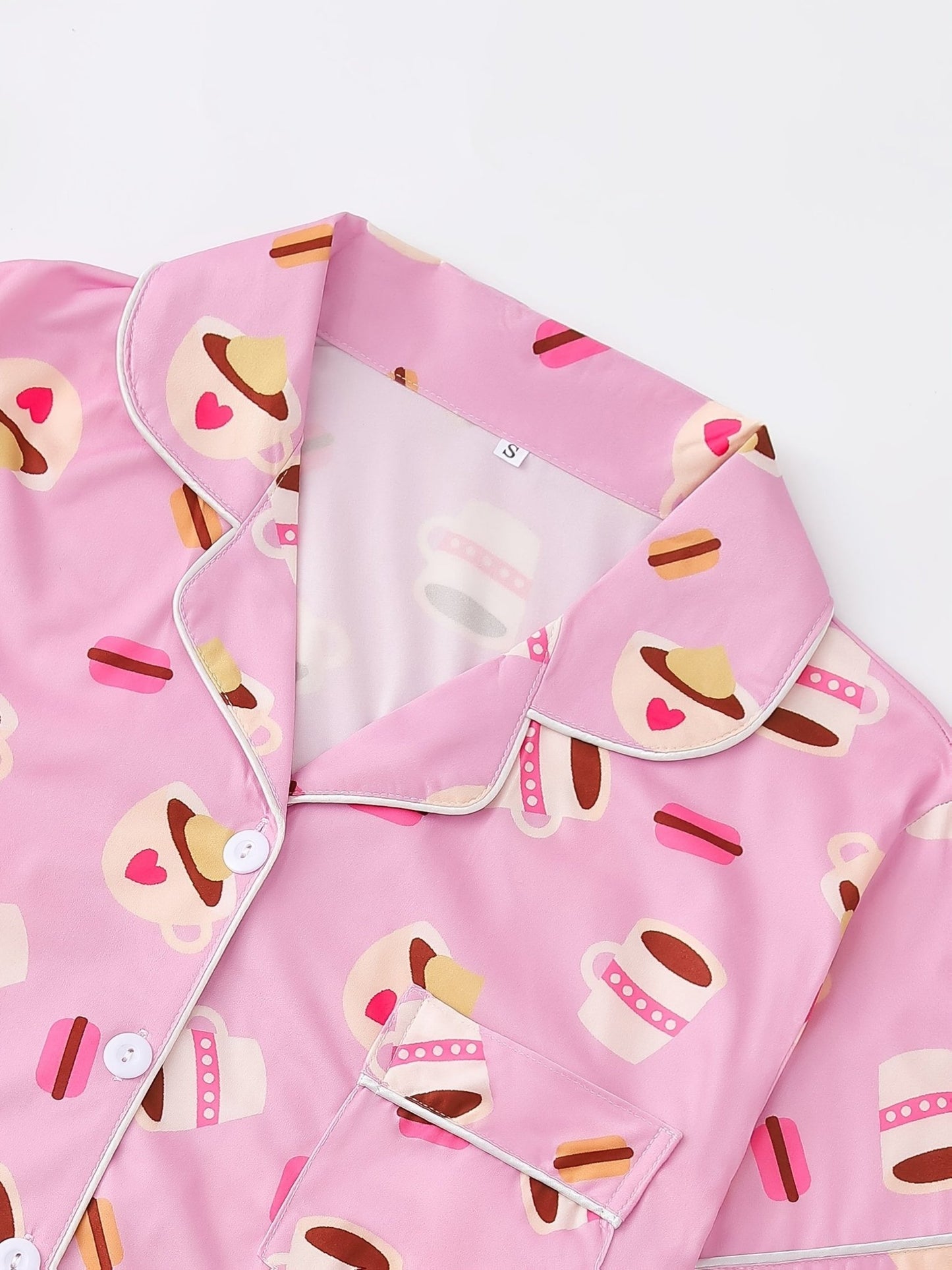 Pink satin-look short-sleeve pajama set with coffee cup and macaron print, piped trim, chest pocket and elastic waist shorts in 95% Polyester 5% Elastane — silky stretch travel-ready loungewear