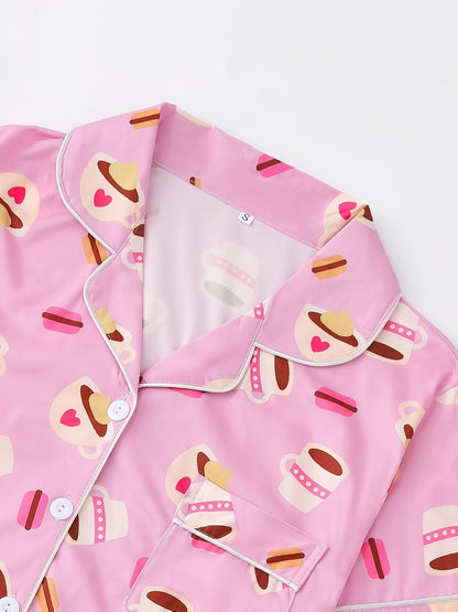 Pink satin-look short-sleeve pajama set with coffee cup and macaron print, piped trim, chest pocket and elastic waist shorts in 95% Polyester 5% Elastane — silky stretch travel-ready loungewear