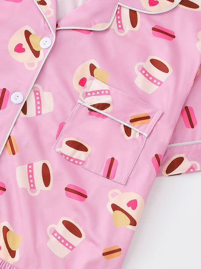 Pink satin-look short-sleeve pajama set with coffee cup and macaron print, piped trim, chest pocket and elastic waist shorts in 95% Polyester 5% Elastane — silky stretch travel-ready loungewear