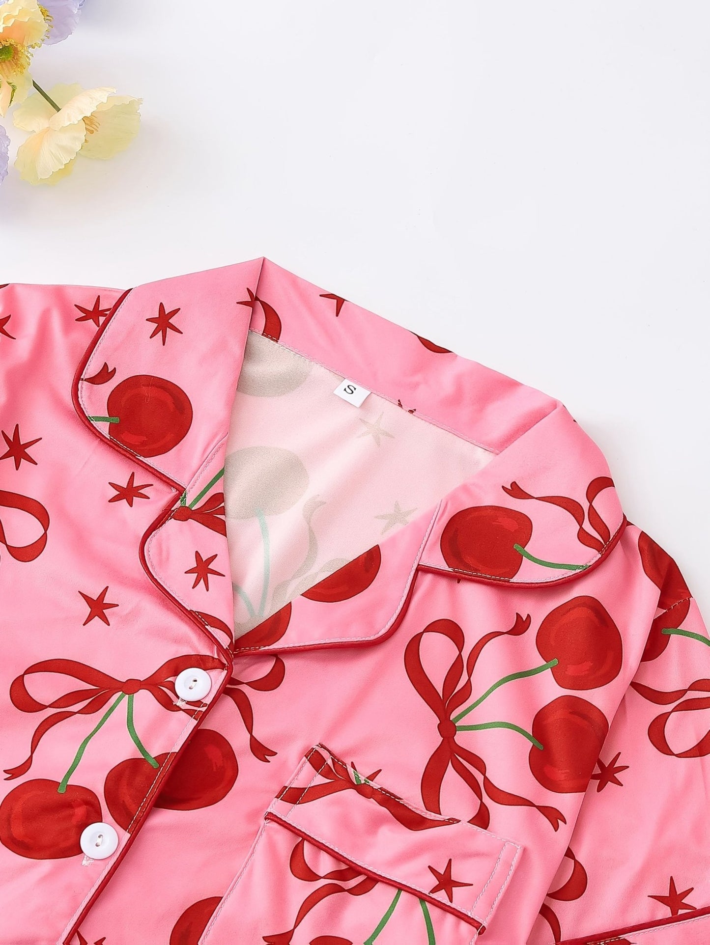 Pink satin-look short-sleeve pajama set with red cherry and bow print, piped trim, chest pocket and elastic waist shorts in 95% Polyester 5% Elastane