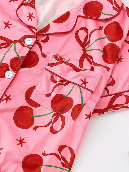 Pink satin-look short-sleeve pajama set with red cherry and bow print, piped trim, chest pocket and elastic waist shorts in 95% Polyester 5% Elastane